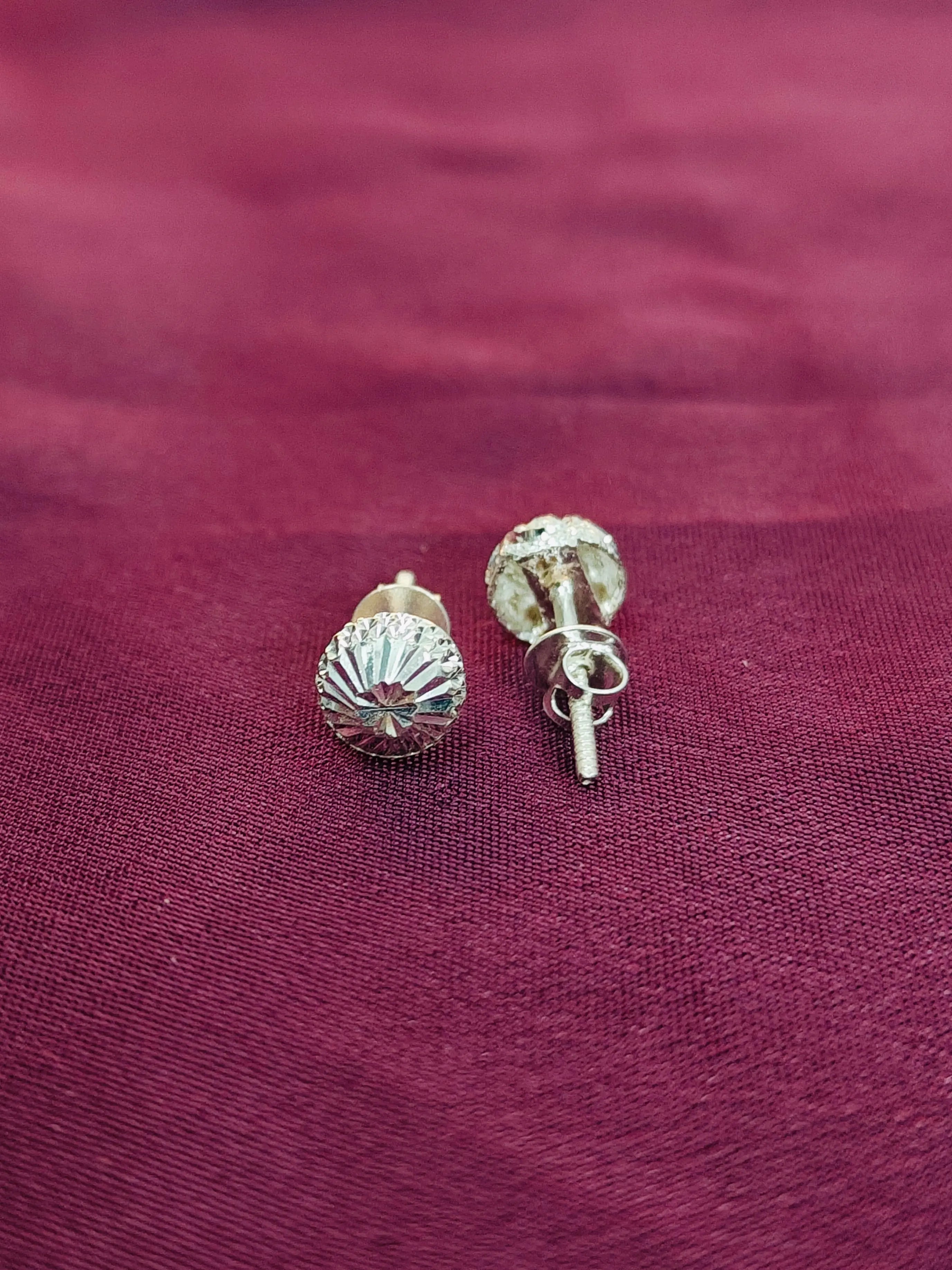 Silver stud earrings on a maroon fabric background